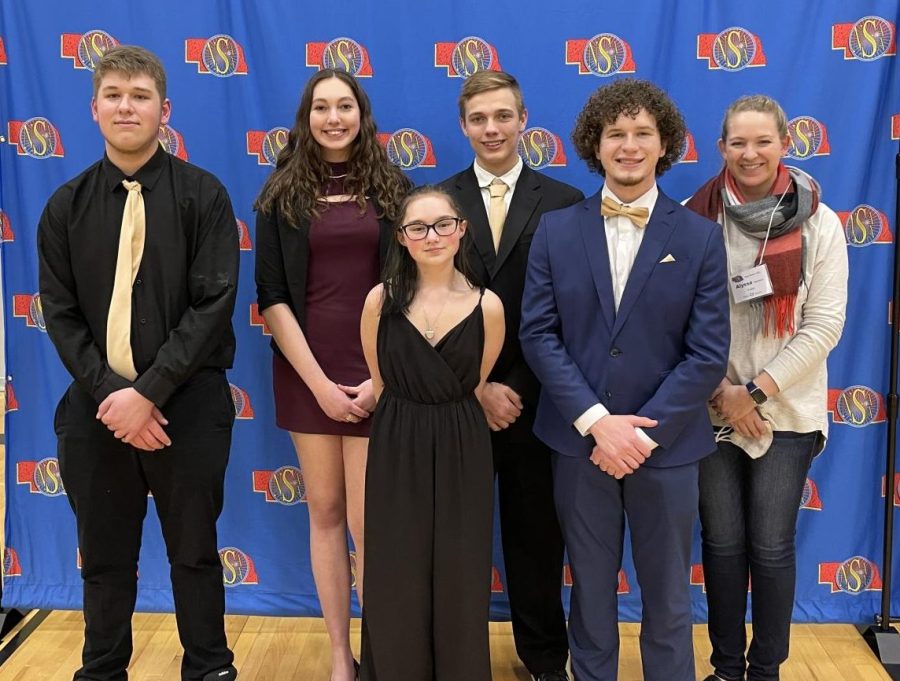 Seniors Caelin WIngender and Mia Dyer, Juniors Tristen Honke and Josh Fisher, graduate Kaden Hufstedler and speech coach Alyssa Hansen stand infront of NSAA banner at State Speech. The group performed How to Kiss a Girl as their OID.