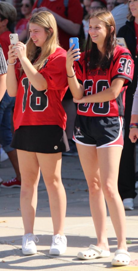 Seniors Taylor Novak and Alexis Polak take pictures of the homecoming parade wearing Yutan football jerseys. Students lined up on the streets of downtown Yutan dressed in spirit gear to watch the parade. “The fact that small towns do parades and everyone gets to decorate floats, it’s really cool and fun,” Polak said. 
