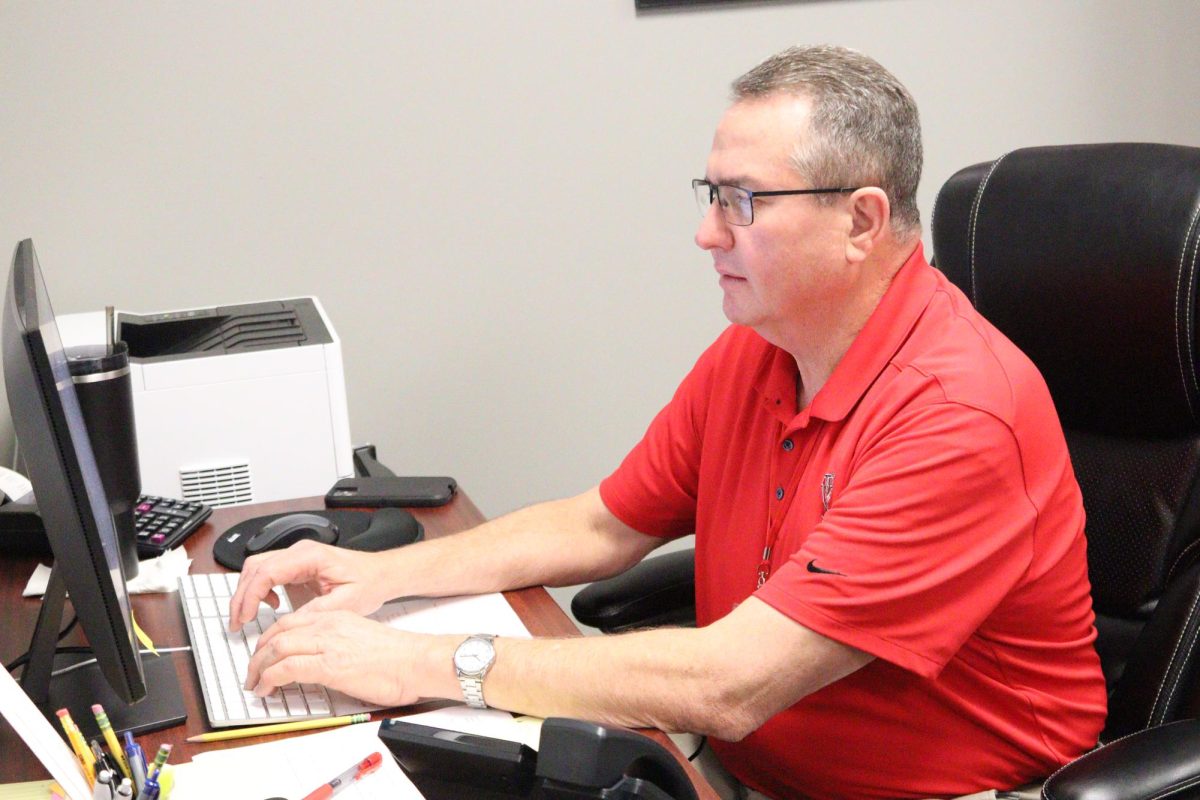 Superintendent Rex Pfeil answers an district related email using the computer. Pfeil states one of the first things he does in the morning is answer emails. The rest of his day consists of staff meetings or following up on tasks that need to get done in the district.