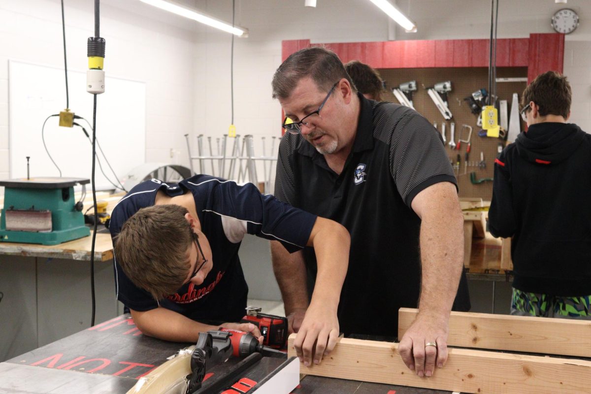 Skilled and Technical Sciences teacher, Brian Fitzgerald assists a student in his Construction Trades class. Students are currently building cornhole games.