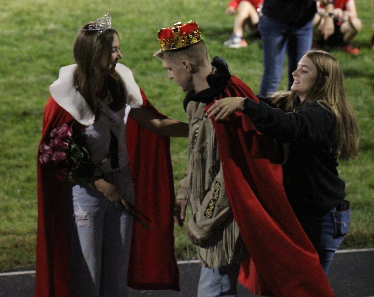 Senior Maura Tichota and graduate Abby Keiser help place the kings cape on senior Ollie Egr after he is crowned.  Keiser was the 2022 queen and was accompanied by graduate Brett Martin, the 2022 king, to help crown the royalty.