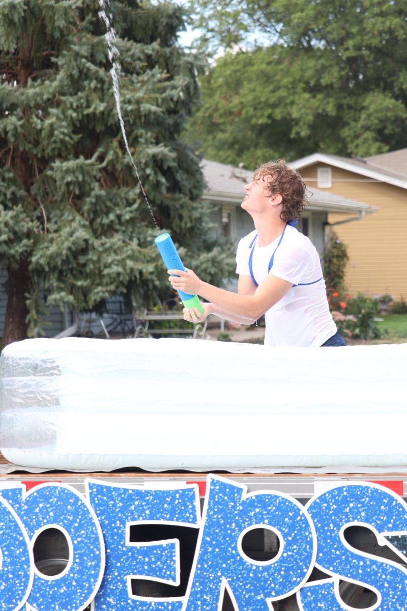 Junior Eli Kult sprays a water gun while riding their class float in the parade. The juniors used water guns to spray the little kids throughout the parade route.