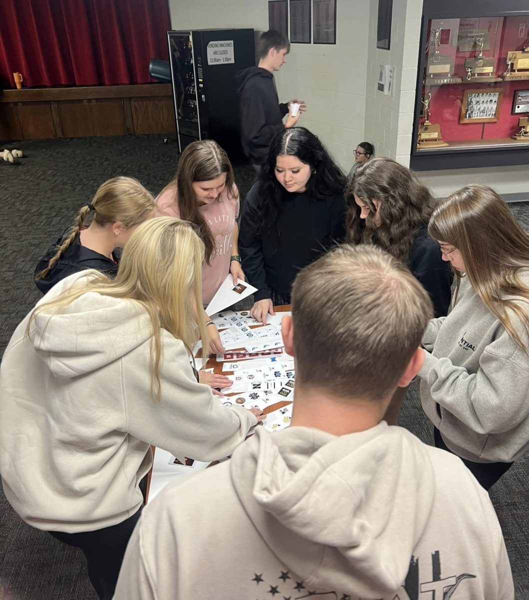 Seniors circle around the table to put college stickers on their pennants. Earlier in the week, each senior took a picture and grabbed stickers of what colleges they were interested in going.